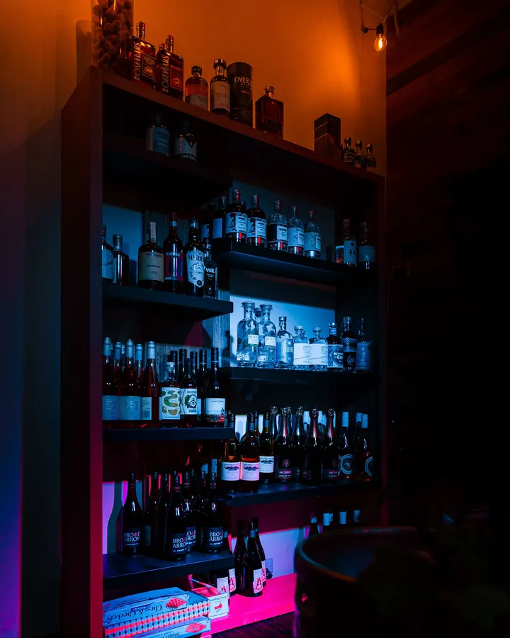 A corner shelf of bottles lit from below in pink, the wall above washed amber.
