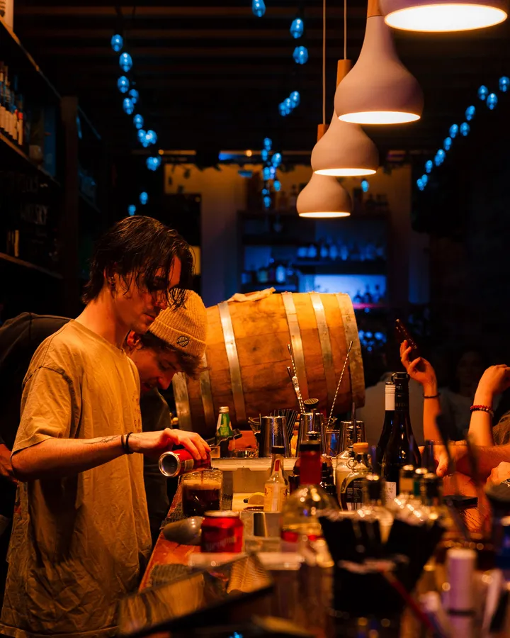 A bartender working beside the barrel, the bar crowded with bottles and glasses.
