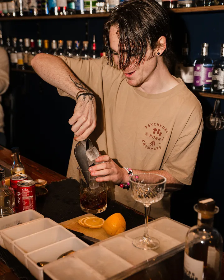 A bartender shaking a drink, lemon wedges and a coupe lined up on the bar.