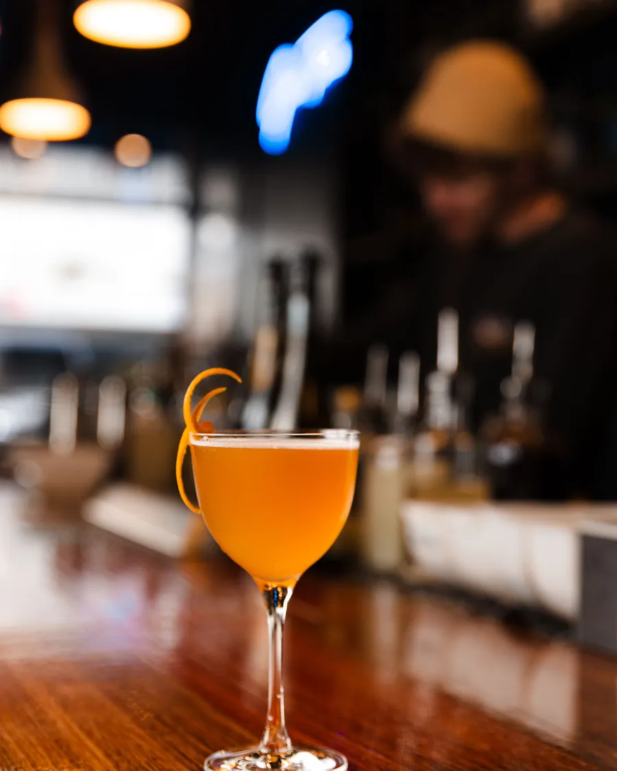 An orange coupe on the bar, the blue Gin Time neon glowing on the wall behind.