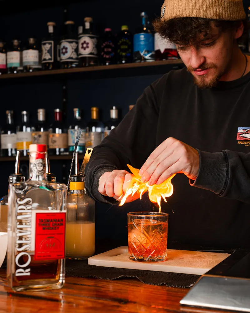 A bartender flaming an orange peel over a drink.