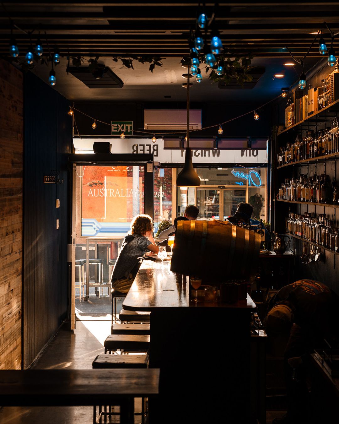 Looking down the long, narrow bar from the back of the room towards the Brisbane Street windows, shelves of bottles glowing amber along the wall.