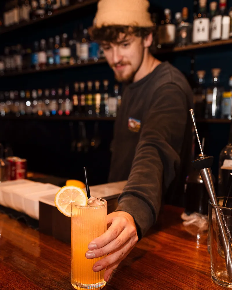 A bartender sliding a highball across the bar.
