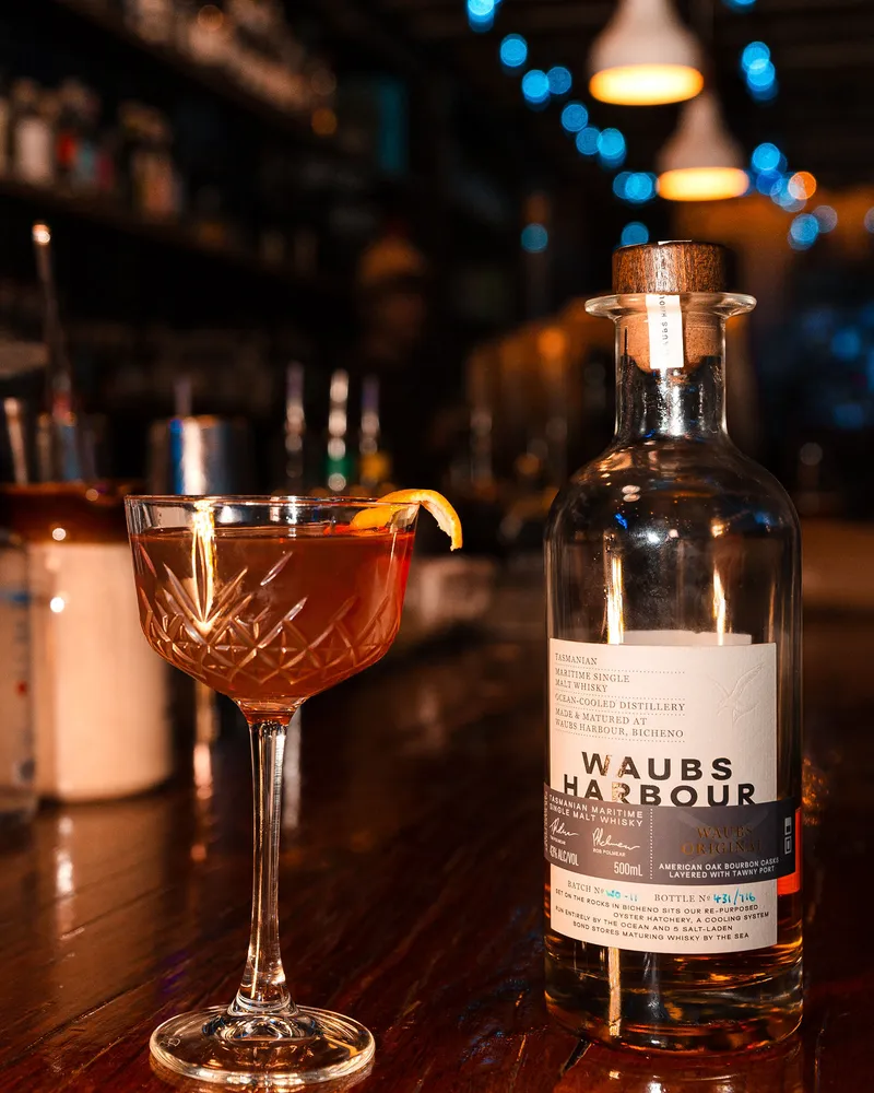 A coupe of something amber beside a bottle of Waubs Harbour whisky on the bar.