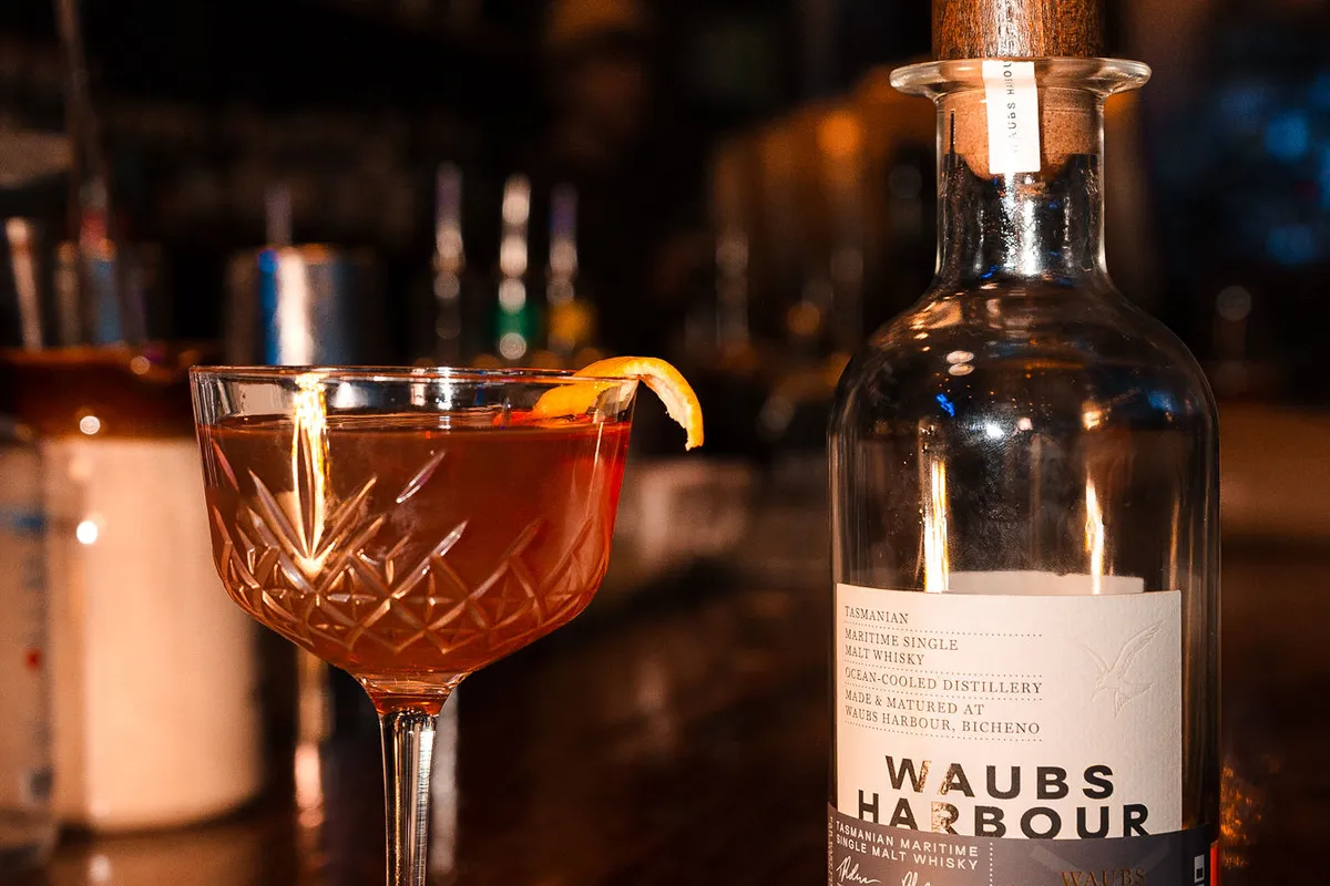 A coupe of something amber beside a bottle of Waubs Harbour whisky on the bar.